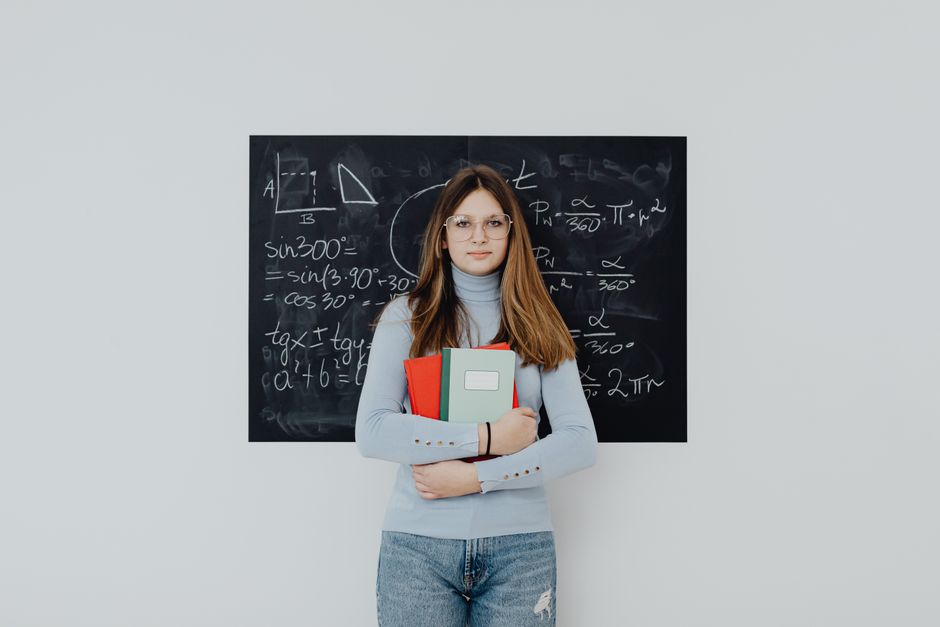 Teenage girl with glasses stands confidently in front of a blackboard with math equations, symbolizing education.